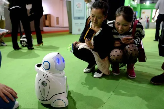 This picture taken on May 14, 2014 shows visitors looking at a domestic robot during the 17th China Beijing International High-Tech Expo (CHITEC) in Beijing. China Beijing International High-Tech Expo (CHITEC) is a major national hi-tech expo that takes place every May in Beijing. (Photo by AFP Photo)