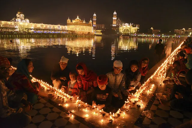 Sikh devotees light candles at the illuminated Golden Temple, the holiest of Sikh shrines, on the birth anniversary of Guru Nanak in Amritsar, India, Tuesday, November 12, 2019. Sikhs across the world are marking the birth anniversary of Guru Nanak, the founder of Sikhism and first guru. (Photo by Prabhjot Gill/AP Photo)