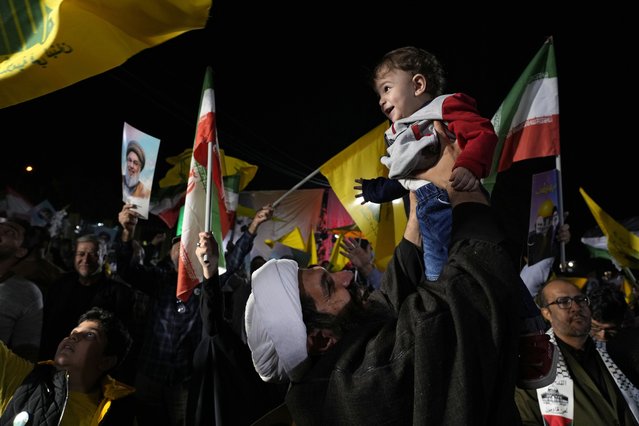 A cleric holds up his son as he celebrates Iran's missile strike against Israel during an anti-Israeli protest at Felestin (Palestine) Square in Tehran, Iran, Tuesday, October 1, 2024. (Photo by Vahid Salemi/AP Photo)