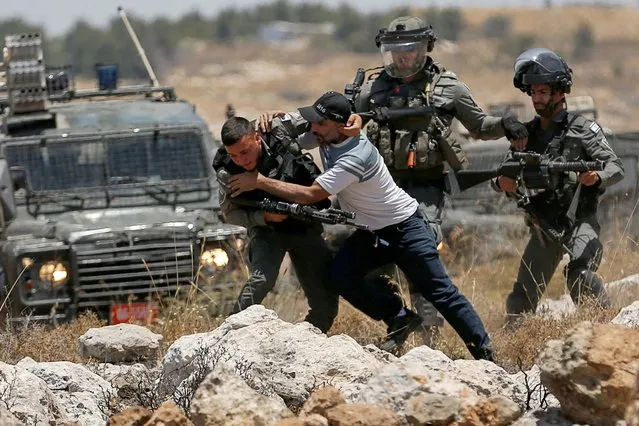 A Palestinian man scuffles with Israeli forces during a protest against Israeli settlement activity near Hebron in the Israeli-occupied West Bank on June 11, 2022. (Photo by Mussa Qawasma/Reuters)