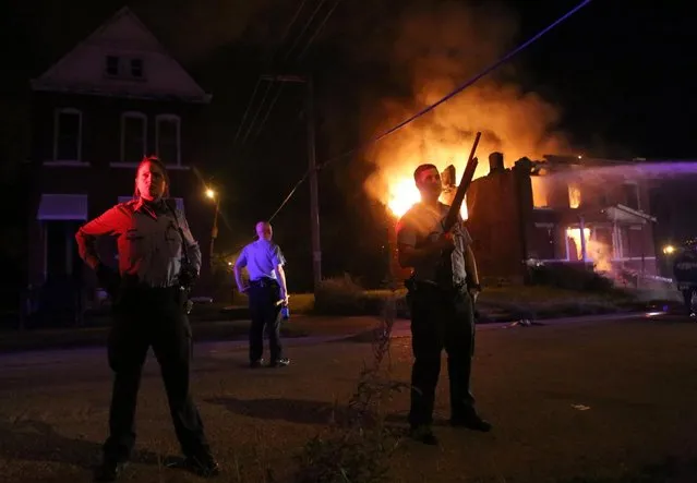 Police stand guard as firefighters extinguish a vacant house that was set on fire during protests following a fatal officer-involved shooting Wednesday, August 19, 2015, in St. Louis. A black 18-year-old fleeing from officers serving a search warrant at a home in a crime-troubled section of St. Louis was fatally shot Wednesday by police after he pointed a gun at them, the city's police chief said. (Photo by Laurie Skrivan/St. Louis Post-Dispatch via AP Photo)