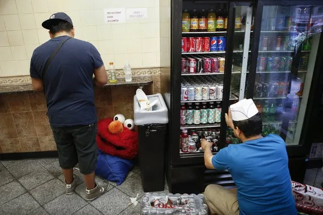 Jorge, an immigrant from Mexico, who works for tips dressed as the Sesame Street character Elmo takes a lunch break in Times Square, New York July 30, 2014. (Photo by Eduardo Munoz/Reuters)