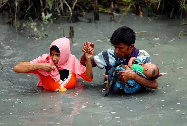 Rohingya refugees carry their child as they walk through water after crossing border by boat through the Naf River in Teknaf, Bangladesh on September 7, 2017. (Photo by Mohammad Ponir Hossain/Reuters)