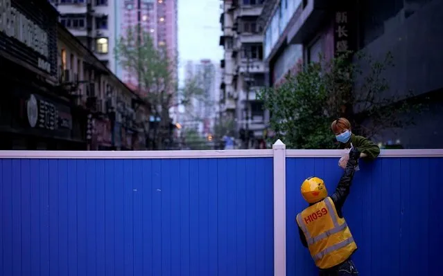 A delivery worker passes food to a woman over barriers blocking an entrance to a residential area in Wuhan, Hubei province, the epicenter of China's coronavirus disease (COVID-19) outbreak, March 28, 2020. (Photo by Aly Song/Reuters)