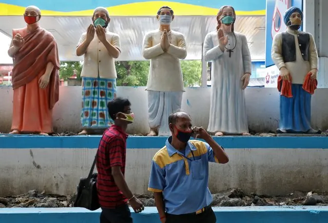 Men wearing protective masks move past the figures with face masks installed outside a fuel station to create awareness about wearing masks to prevent the spreading of the coronavirus disease (COVID-19), in Kolkata, India, May 1, 2020. (Photo by Rupak De Chowdhuri/Reuters)