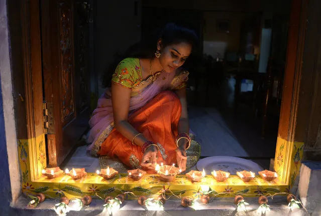 An Indian woman Nikitha places earthen lamps or “diyas” at the entrance of her home on the eve of Diwali Festival in Hyderabad on October 18, 2017. Diwali, the Hindu festival of lights, marks the triumph of good over evil, and commemorates the return of Hindu deity Rama to his birthplace Ayodhya after victory against the demon king Ravana. (Photo by Noah Seelam/AFP Photo)