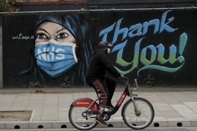 A man wearing a face mask cycles past a recently painted piece of street art by The Artful Dodger (A. Dee) entitled “NHS Dedication Mural”, thanking national health service workers, during the coronavirus lockdown in the Elephant and Castle area of London, Sunday, May 3, 2020. The highly contagious COVID-19 coronavirus has impacted on nations around the globe, many imposing self isolation and exercising social distancing when people move from their homes. (Photo by Matt Dunham/AP Photo)