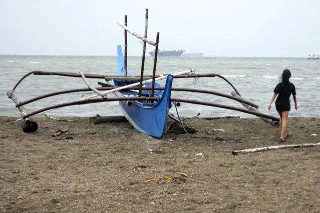 A girl walks past a boat that was placed on higher ground as they prepare for the approach of Typhoon Noru at the seaside slum district of Tondo while Typhoon Noru approaches Manila, Philippines, Sunday, September 25, 2022. (Photo by Aaron Favila/AP Photo)