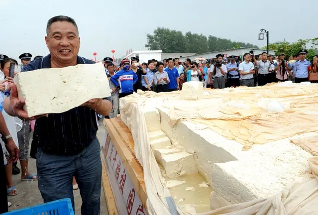 A man holds a piece of the eight-ton tofu, during an event in Huainan, Anhui province, September 15, 2015. Thousands of visitors had a share of the tofu made by 50 workers together in seven hours, according to local media. (Photo by Reuters/China Daily)