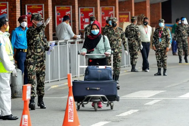 A Nepali migrant worker previously stranded in Kuwait (C) due to restrictions imposed as a preventive measure against the spread of the COVID-19 coronavirus pushing her luggage on a cart arrives as security personnel guide her at the Tribhuvan International airport in Kathmandu on June 11, 2020. (Photo by Prakash Mathema/AFP Photo)