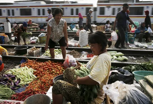 A vendor serves a customer at a vegetable market as a commuter train passes in Jakarta, October 2, 2015. (Photo by Reuters/Beawiharta)
