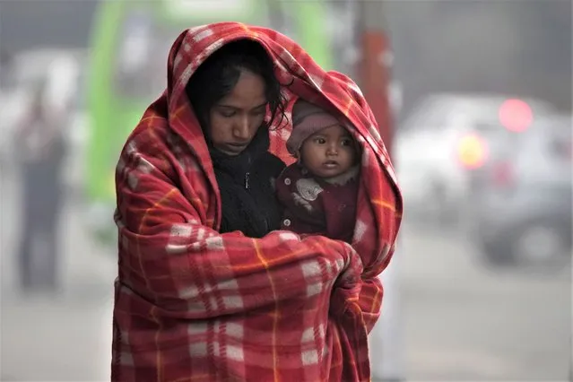 A homeless woman carries her child, both wrapped in a blanket, on a cold and foggy morning in Jammu, India, Tuesday, December 27, 2022. (Photo by Channi Anand/AP Photo)