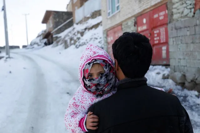 An Afghan man holds his child as he walks on a snow-covered street on the TV mountain in Kabul, Afghanistan on January 25, 2023. (Photo by Ali Khara/Reuters)