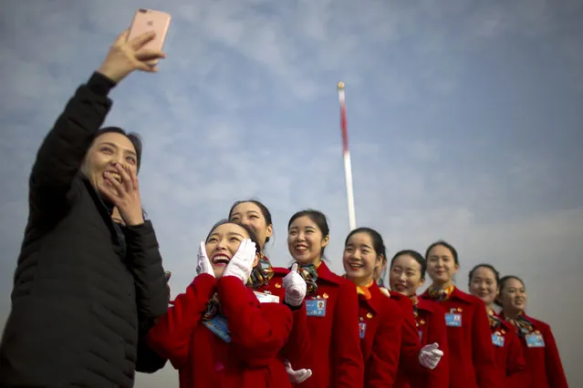 Hospitality staff members react after posing for a selfie during the opening session of China's National People's Congress (NPC) at the Great Hall of the People in Beijing, Monday, March 5, 2018. China's government pledged Monday to deliver robust growth, pursue advanced technology and boost military spending while urging the public to embrace President Xi Jinping's rule as its ceremonial legislature prepared for changes to allow him to stay in power indefinitely. (Photo by Mark Schiefelbein/AP Photo)