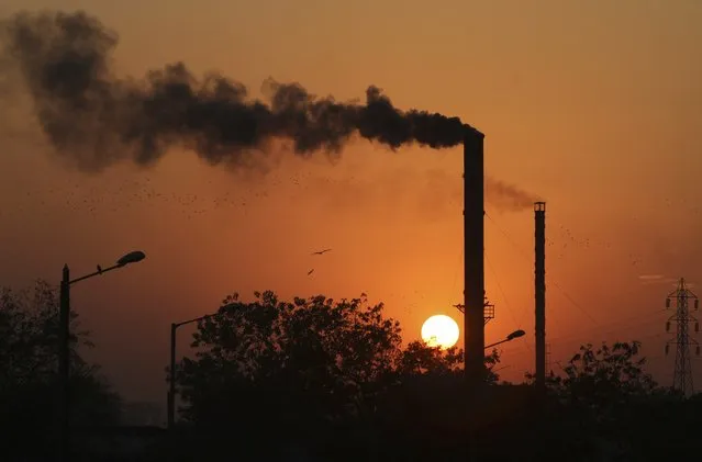 Birds fly past at sun set as smoke emits from a chimney at a factory in Ahmadabad, India, Monday, December 8, 2014. The momentum from a historic U.S.-China pact to resist global warming is showing signs of fading at the U.N. climate talks in Peru as the familiar rich-poor conflict persists over who should do what to keep the planet from overheating. The conference's high-level phase begins Tuesday. (Photo by Ajit Solanki/AP Photo)