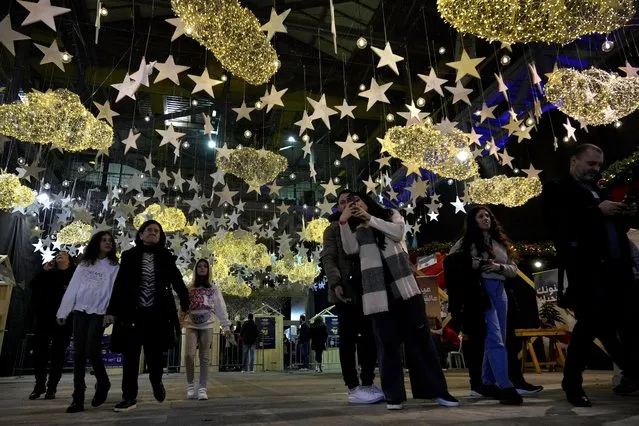 People walk past Christmas decorations at a Christmas market in Beirut, Lebanon, Wednesday, December 21, 2022. The economic crisis has forced a drastic lifestyle change for most of the country, struggling to afford skyrocketing costs for Christmas gifts, presents, and celebrations the way they once did. (Photo by Bilal Hussein/AP Photo)