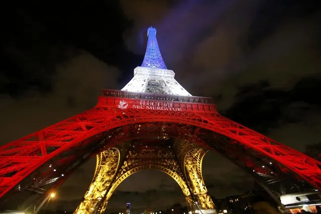 The Eiffel Tower is lit with the blue, white and red colours of the French flag in Paris, France, November 17, 2015, to pay tribute to the victims of a series of deadly attacks on Friday in the French capital. The City of Paris motto "Fluctuat Nec Mergitur", Latin for "buffeted (by waves) but not sunk" is projected on the Eiffel Tower. (Photo by Jacky Naegelen/Reuters)