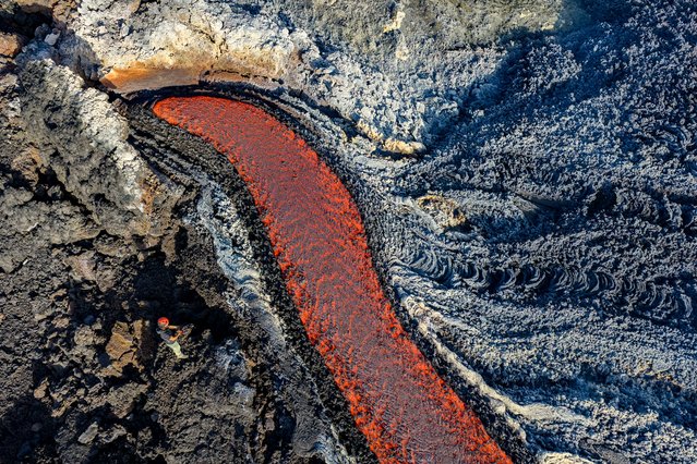 This aerial view shows a man standing near a flow of lava on the Mount Etna volcano (Torre del Filosofo - Etna Sud) on August 28, 2025. The Etna volcanic eruption started on August 10 and remained active the last weeks. (Photo by Giuseppe Distefano/AFP Phoot)