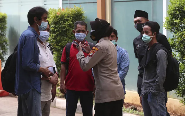 An Indonesian police talks to relatives of passengers of a Sriwijaya Air jet crashed into the sea as they arrive at a hospital in Jakarta, Indonesia, Tuesday, January 12, 2021. Indonesian navy divers were searching through plane debris and seabed mud Tuesday looking for the black boxes of the jet that nosedived into the Java Sea over the weekend with 62 people aboard. (Photo by Achmad Ibrahim/AP Photo)