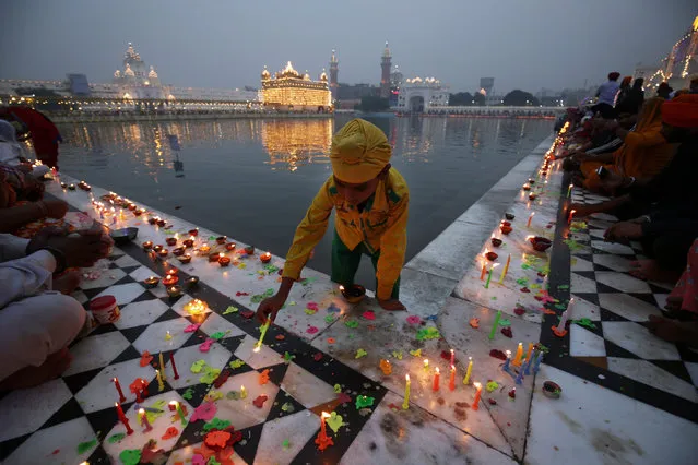 A Sikh boy lights candles near the sacred pond at the Golden Temple, the holiest of Sikh shrines, on the occasion of Diwali festival and Bandi Chorh Diwas in Amritsar, India, 30 October 2016. Devotees started to visit the Golden Temple from pre-dawn hours to seek blessings on Diwali festival. The festival coincides with the Bandi Chorh Diwas which is also celebrated at the Golden Temple to mark the return of Guru Hargobind, the sixth Guru or the Master of the Sikhs, to Amritsar after his release from Gwalior fort during the reign of Mughal emperor Jahangir. (Photo by Raminder Pal Singh/AFP Photo)