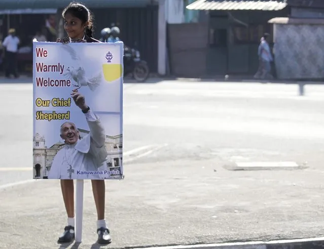 A girl holds a sign to welcome Pope Francis as she waits on the road for the pope's arrival at Colombo airport January 13, 2015. Pope Francis said on Tuesday Sri Lanka needed to find out the truth of what happened during its long civil war in order to consolidate peace and heal scars between religious communities. (Photo by Dinuka Liyanawatte/Reuters)