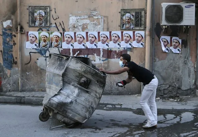 A protester takes cover behind a garbage bin as posters of Sheik  Ali Salman, head of Bahrain's main opposition party Al Wefaq, are seen on a wall during clashes in the village of Bilad Al Qadeem, south of Manama January 20, 2015. (Photo by Hamad I. Mohammed/Reuters)