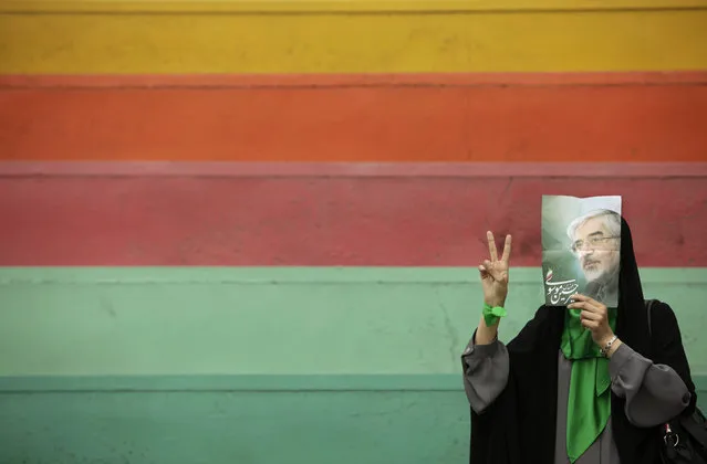 A supporter of main challenger and reformist candidate Mir Hossein Mousavi, not wanting to be photographed, hides her face using a poster of him as she waits in the stands at an election rally at the Heidarnia stadium in Tehran, Iran, Tuesday, June 9, 2009. (AP Photo/Ben Curtis)