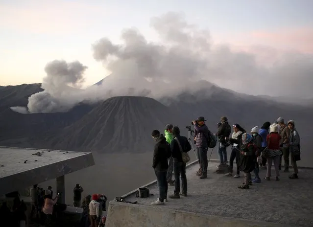 Tourists watch the sun rise as Mount Bromo erupts in the background near Ngadisari, Probolinggo, East Java, Indonesia January 6, 2016. (Photo by Darren Whiteside/Reuters)