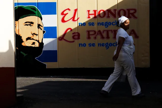 An employee of a state-owned candy store turns around while walking past a painting depicting Cuba's former President Fidel Castro and the writing reading “Honor is not negotiable, the fatherland is not negotiable”, following the announcement of his death, in Havana, Cuba, November 27, 2016. (Photo by Reuters/Stringer)