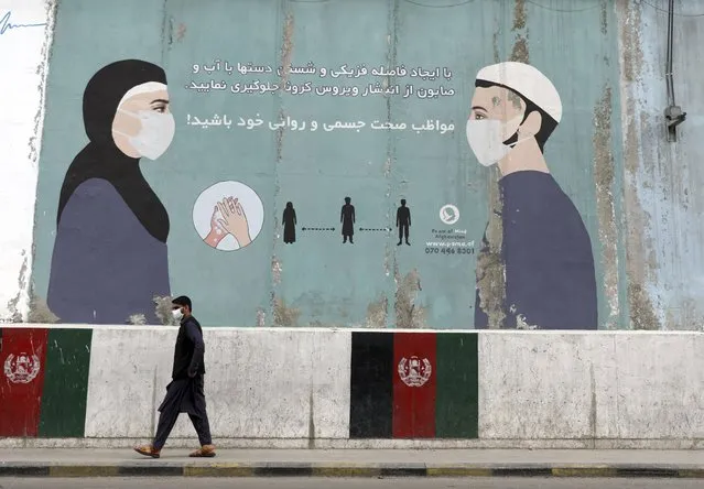 A man wearing a protective face mask to help curb the spread of the coronavirus, walks past a painted wall of Ministry of Public Health, which guides social distancing in Kabul, Afghanistan, Saturday, May 29, 2021. (Photo by Rahmat Gul/AP Photo)