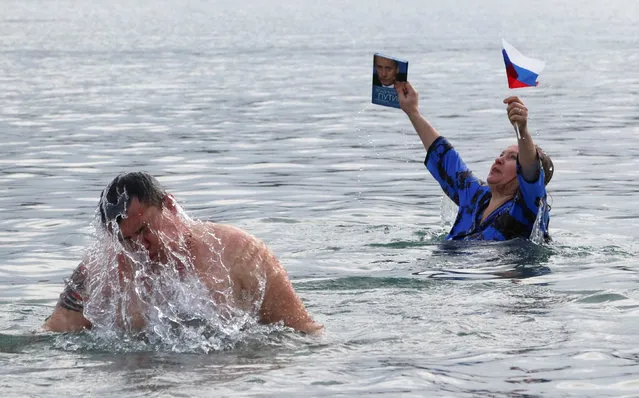 A supporter of Russian President Vladimir Putin holds a flag while standing in the waters of Karantinnaya Bay during celebrations of the Orthodox Christian feast of Epiphany in the Black Sea port of Sevastopol, Crimea on January 19, 2019. (Photo by Pavel Rebrov/Reuters)