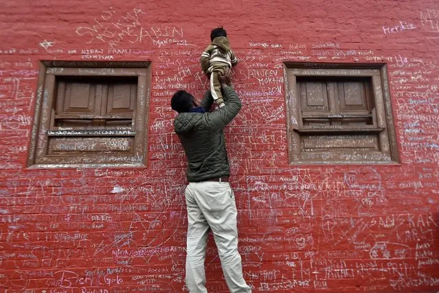 A child helped by his father writes a message with chalk on a wall at the Saraswati temple on the occasion of the Hindu festival of “Basanta Panchami”, in Kathmandu on February 14, 2024. (Photo by Prakash Mathema/AFP Photo)