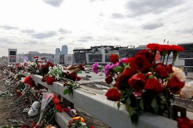 Flowers are placed on the roadside in front of the burnt-out Crocus City Hall following a deadly attack on the concert venue on the outskirts of Moscow, Russia on March 26, 2024. (Photo by Evgenia Novozhenina/Reuters)