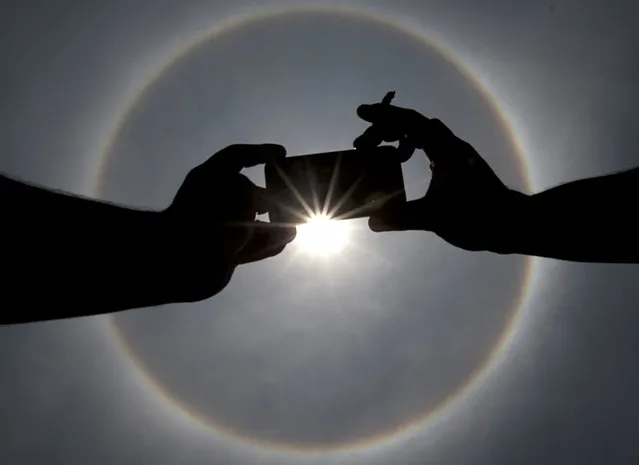 A man uses his mobile phone to photograph a circular sun halo in Mexico City, Thursday, May 21, 2015. The ring around the sun is a fairly common weather phenomenon caused by ice crystals in the upper atmosphere. (Photo by Marco Ugarte/AP Photo)