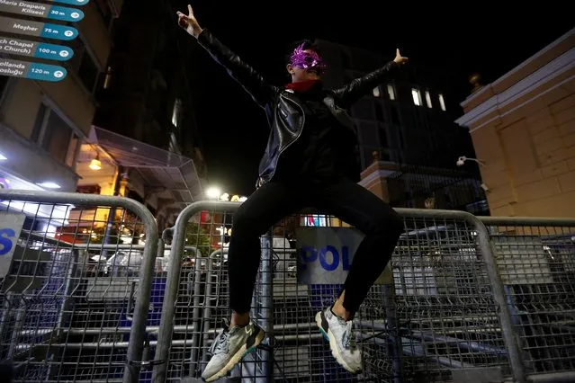 A demonstrator in a mask climbs a police barricade during a protest against gender-based violence on the International Day for the Elimination of Violence Against Women, in Istanbul, Turkey on November 25, 2021. (Photo by Dilara Senkaya/Reuters)