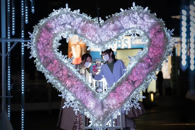 Women wearing face masks check their phones after taking a selfie photograph next to a Christmas display on December 21, 2021 in Tokyo, Japan. Tokyo Metropolitan Government reported 38 new coronavirus cases today while fewer than 70 Omicron infections have been recorded so far in the country. (Photo by Carl Court/Getty Images)