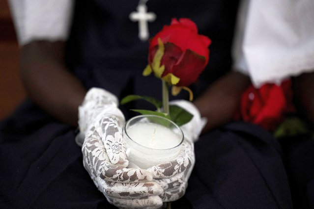 A girl holds a candle during her first communion ceremony at the Our Lady of the Assumption Cathedral in Cap-Haitien, Haiti on April 28, 2024. (Photo by Ricardo Arduengo/Reuters)