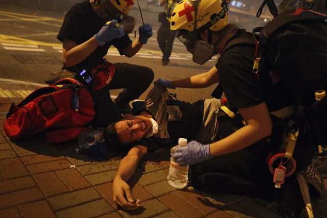 Medical workers help a protester in pain from tear gas fired by policemen on a street in Hong Kong, Sunday, July 21, 2019. Hong Kong police have thrown tear gas canisters at protesters after they refused to disperse. Hundreds of thousands of people took part in a march Sunday to call for direct elections and an independent investigation into police tactics used during earlier pro-democracy demonstrations. Police waved a black warning flag Sunday night before lobbing the canisters into a crowd of protesters. (Photo by Bobby Yip/AP Photo)