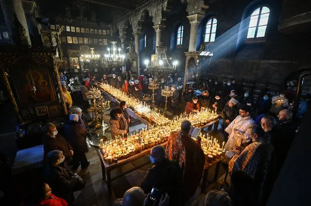 Believers pray around a cross-shaped platform covered with candles attached to jars of honey during a ceremony marking the day of Saint Haralampi, Orthodox patron saint of beekeepers, at the Church of the Blessed Virgin in Blagoevgrad, eastern Bulgaria, on February 10, 2022. (Photo by Nikolay Doychinov/AFP Photo)