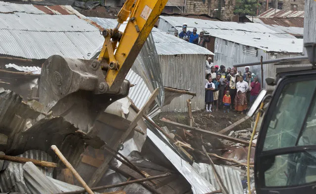 Residents look across as a mechanical digger demolishes their neighbors' shacks on the other side of the river, close to the site of last week's building collapse, after their homes were deemed unfit for habitation, in the Huruma neighborhood of Nairobi, Kenya Friday, May 6, 2016. (Photo by Ben Curtis/AP Photo)