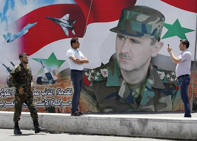 A man takes a photo of his friend in front of a poster of Syria's President Bashar al-Assad at Umayyad Square in Damascus May 16, 2014. Syria is holding a presidential election for June 3, preparing the ground for Assad to defy widespread opposition and extend his grip on power, days after he said the civil war was turning in his favour. Opponents have dismissed the vote as a farce. (Photo by Khaled al-Hariri/Reuters)