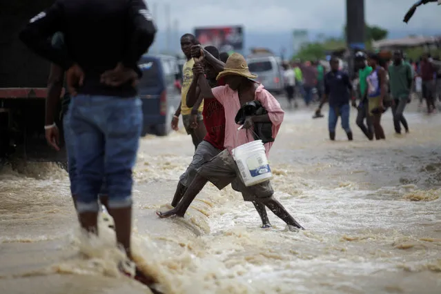 A youth helps an elder to pass a flooded area along National Road #2 in Leogane, Haiti, May 27, 2016. (Photo by Andres Martinez Casares/Reuters)