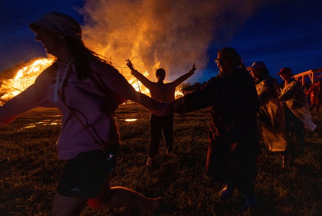 People dance in a circle near a burning installation during the Archstoyanie 2024 festival in the village of Nikola-Lenivets, Kaluga region, Russia on July 27, 2024. (Photo by Maxim Shemetov/Reuters)