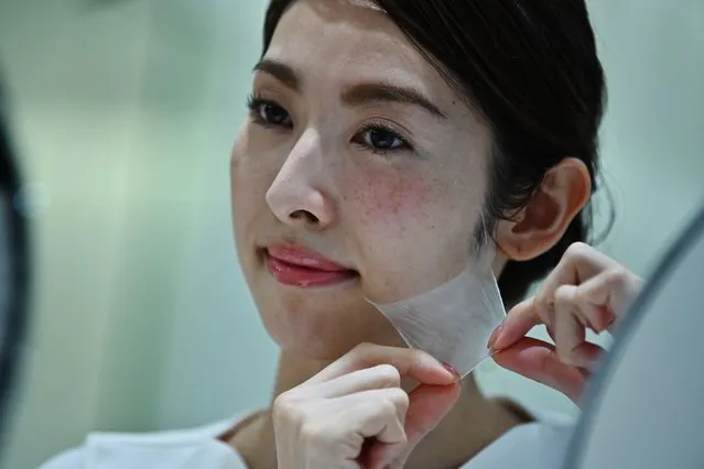 An employee for Japanese cosmetics company Kao removes a super thin transparent layer after using a palm-sized diffuser on her face, during a product demonstration in Tokyo on December 4, 2019. Kao on December 4 unveiled what it said was the world's first spray-on skin, using fibres one-100th the thickness of a human hair to form a membrane covering the face. (Photo by Charly Triballeau/AFP Photo)