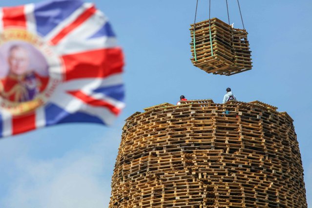 Bonfire builders top off the 11th night bonfire on the Craigyhill estate in Larne, Northern Ireland on July 8, 2023, claimed to be the tallest in the world by the builders. The bonfire, will be lit in the annual commemoration of the victory of Protestant King William III of Orange against Catholic King James II at the battle of the Boyne on July 12, 1690. (Photo by Paul Faith/AFP Photo)