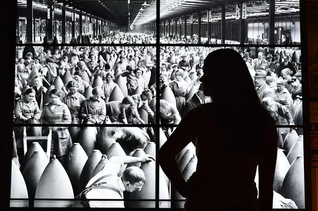 A woman looks at a projected stills image of a 1915 British munitions factory during a photocall to launch the Imperial War Museum's new First World War Galleries Atrium in London, on July 16, 2014. The First World War Galleries tell the story of the war and feature over 1,300 objects from diaries and personal mementos through to weapons, posters and film. The exhibition opens to the public on July 19, 2014. (Photo by Ben Stansall/AFP Photo)