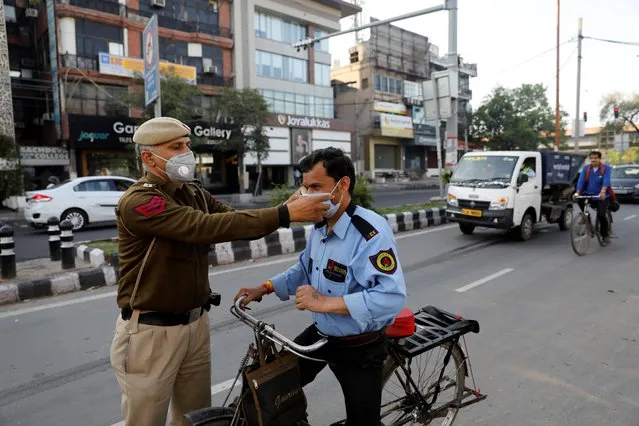 A policeman adjusts the mask of a security guard during a lockdown amid a coronavirus disease (COVID-19) outbreak in New Delhi, India, March 25, 2020. (Photo by Adnan Abidi/Reuters)