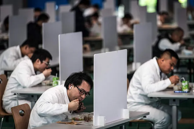 This photo taken on April 7, 2020 shows employees eating during a lunch break at an auto plant of Dongfeng Honda in Wuhan in China's central Hubei province. Thousands of relieved citizens streamed out of China's Wuhan on April 8 after authorities lifted months of lockdown at the coronavirus epicntre, offering some hope to the world despite record deaths in Europe and the United States. (Photo by AFP Photo/China Stringer Network)