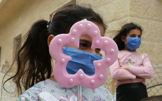 Girls wearing face masks and one of them holds a candle as they wait for the blessing of a priest roaming neighbourhoods to celebrate Palm Sunday, amid the lockdown to contain the coronavirus disease (COVID-19), in Marjayoun, southern Lebanon on April 5, 2020. (Photo by Aziz Taher/Reuters)