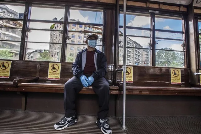 A man sits on a tram as signs reading “please don't sit here, respect social distancing”, are displayed on the benches, in Milan, Italy, Wednesday, April 29, 2020. Italian factories, construction sites and wholesale supply businesses can resume activity as soon as they put safety measures into place aimed at containing contagion with COVID-19. (Photo by Luca Bruno/AP Photo)
